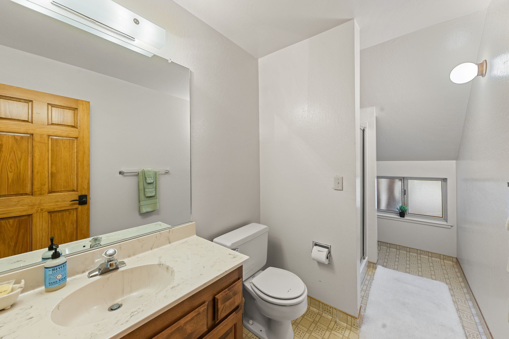 A bathroom with a wooden door, a white sink, a toilet, and a small window with a plant.