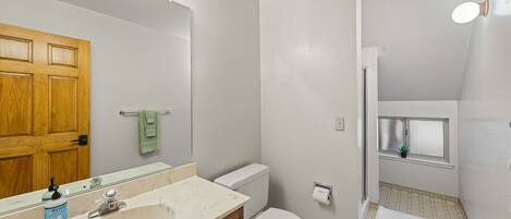 A bathroom with a wooden door, a white sink, a toilet, and a small window with a plant.
