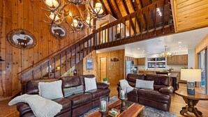 A spacious living room with a large brown leather sofa, a wooden coffee table, and a staircase leading to an upper level. - McKinney Lakeview Lodge in Homewood (Tahoma)