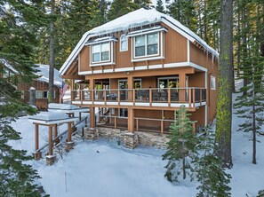 Une cabane en bois à deux étages, dotée d’un balcon, entourée de neige et d’arbres.