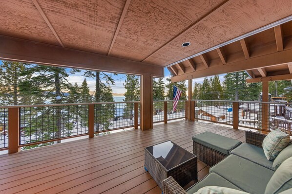 Une terrasse couverte avec un plancher en bois, une table à plateau en verre et un coin salon agrémenté de coussins.
