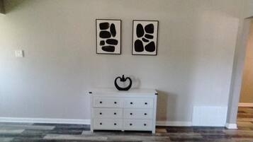 Une pièce avec une commode blanche, deux œuvres d’art abstraites accrochées au mur et un tapis à motifs.