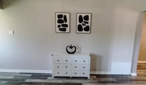A room with a white dresser, two abstract wall art pieces, and a patterned carpet.