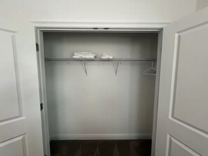 A walk-in closet with a metal rod shelf, two white towels, and a hanger.