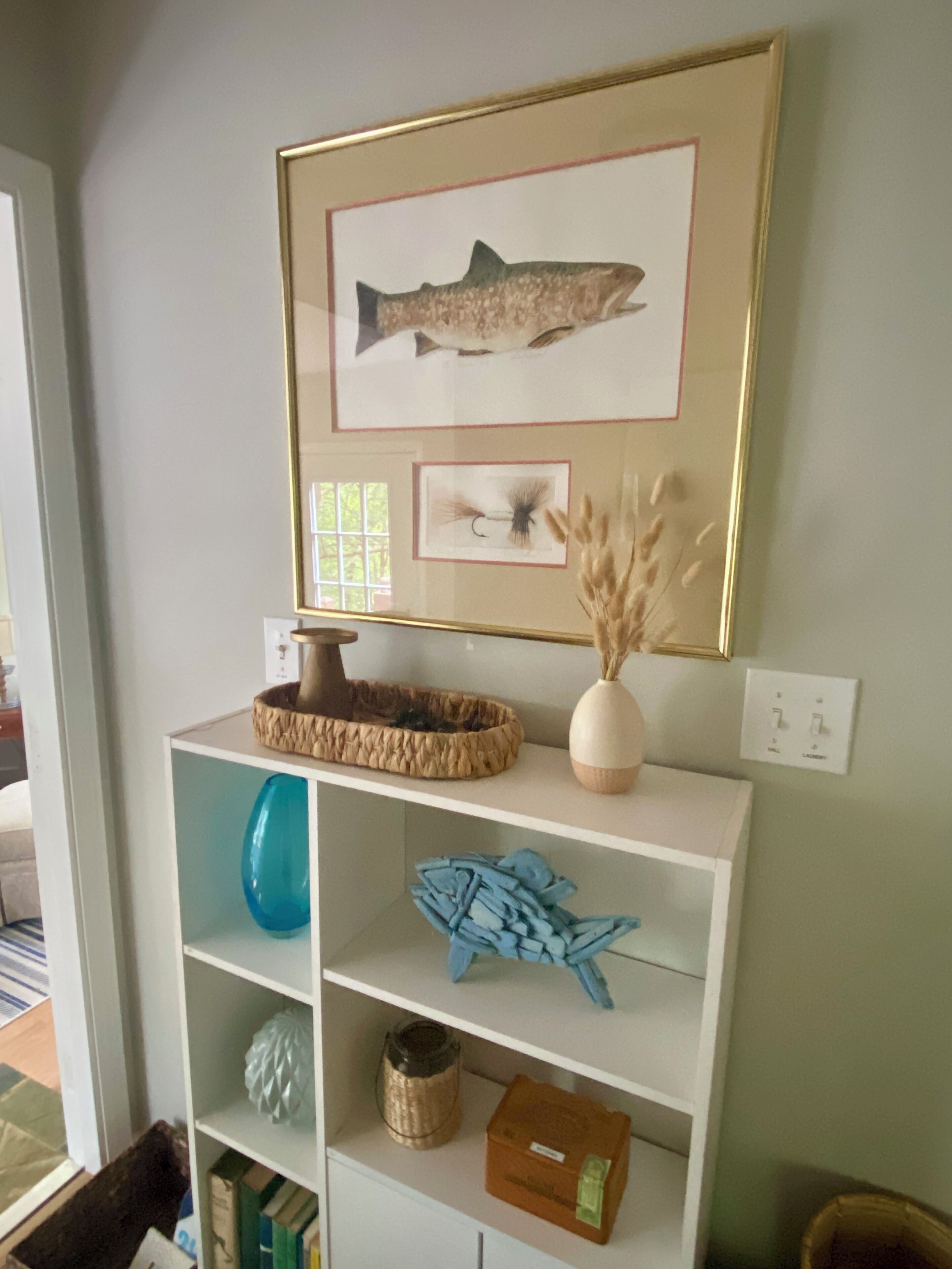 A white shelving unit with a framed fish illustration, a decorative bowl, and a vase.
