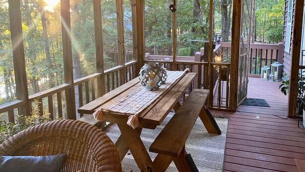 A wooden deck with a picnic table and benches, surrounded by large windows offering a view of the forest.