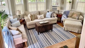 A cozy living room with a beige sofa, a patterned rug, and a wicker ottoman.