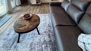 Un salon spacieux avec un haut plafond, un canapé en cuir, une table basse en bois et un tapis.