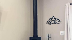 Une cheminée en pierre avec un poêle à bois noir, un extincteur et une décoration de montagne au mur.
