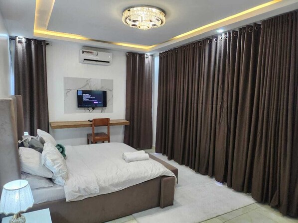 A modern bedroom with a large bed, a desk, a television, and a chandelier.