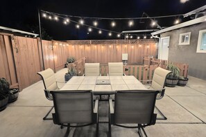 An outdoor patio with a table and chairs, string lights, and wooden fences.