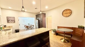 Una cucina moderna con un piano di lavoro in granito, sgabelli da bar, un tavolo da pranzo rotondo e un orologio a parete.