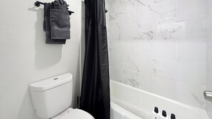 A bathroom with a toilet, a shower curtain, and a tiled wall. - Cozy King Studio | 5 Min to Zoo, JU & DT (Jacksonville)