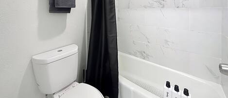 Une salle de bain avec des toilettes, une douche avec un rideau noir et un ventilateur fixé au mur.