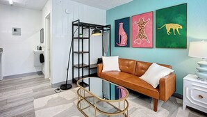 A modern living room with a brown leather sofa, a glass coffee table, and a bookshelf. There are three framed animal prints on the wall. - Cozy King Studio | 5 Min to Zoo, JU & DT (Jacksonville)