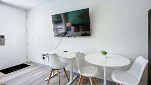 A modern room with a white desk, two white chairs, a small table, and a TV mounted on the wall. - Cozy King Studio | 5 Min to Zoo, JU & DT (Jacksonville)