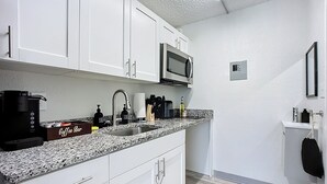 A modern kitchen with white cabinets, a granite countertop, a coffee bar, and a microwave. - Cozy King Studio | 5 Min to Zoo, JU & DT (Jacksonville)
