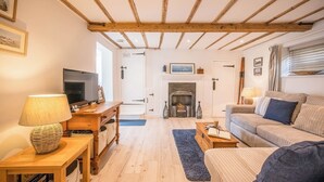 Un salon chaleureux avec une cheminée, des poutres apparentes, un téléviseur et un canapé.