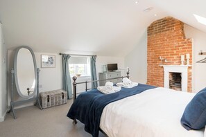 Un dormitorio con cama, espejo, cómoda, ventana con cortinas, chimenea y pared de ladrillo.