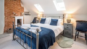 Une chambre avec un mur en briques, un lit avec un cadre en métal, deux tables de chevet avec des lampes et une petite cheminée.