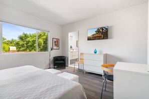 Une chambre d’hôtel moderne avec un grand lit, un bureau et une chaise. Il y a une fenêtre donnant sur des arbres et un tableau accroché au mur.