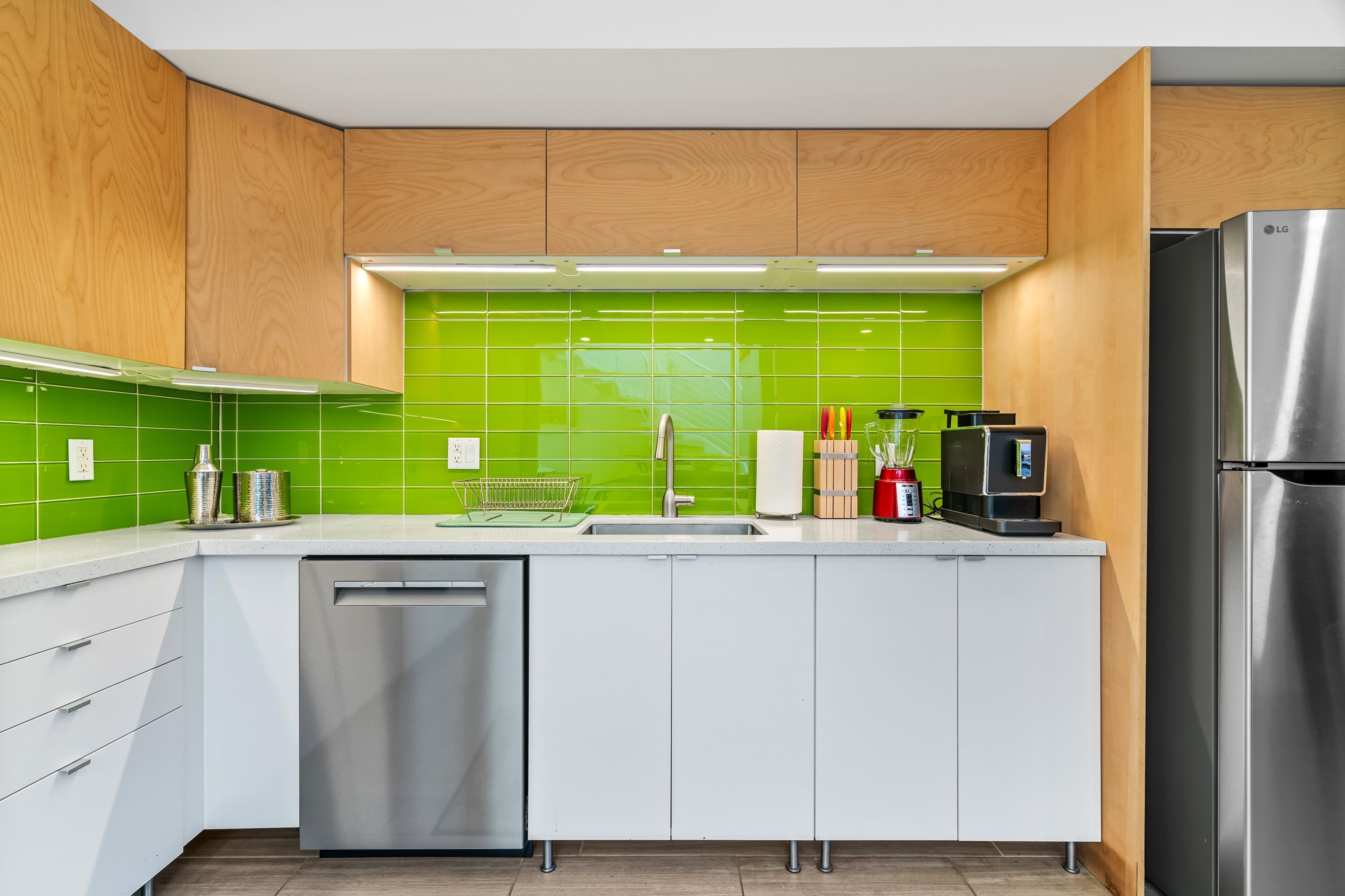 Une cuisine moderne avec des meubles blancs, un pare-feu vert et des appareils électroménagers en acier inoxydable.