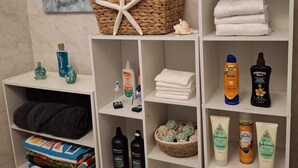 A bathroom with a tiled wall, a starfish decoration, a basket with towels, and shelves with toiletries and towels.