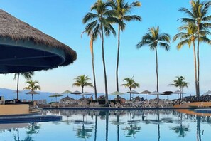 A pool area with lounge chairs and umbrellas, surrounded by palm trees and a thatched roof structure. - "Spacious with beach and restaurant access!" (Puerto Vallarta)