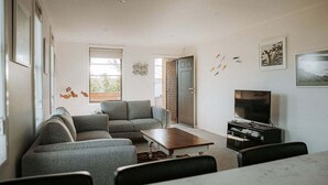 Un salon moderne avec un canapé gris, une table basse en bois, un téléviseur à écran plat et une bibliothèque.