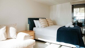 Une chambre moderne avec un lit, une table de chevet, une chaise et une vue à travers une porte vitrée.