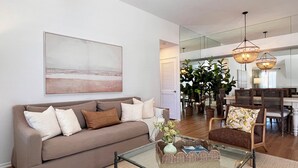 A modern living room with a sofa, coffee table, and dining area. - Luxurious Seabreeze Chic, 2 Bed Condo (Newport Beach)