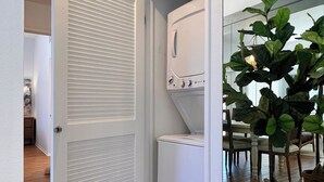A laundry room with a white washer and dryer, a door with a louvered panel, and a potted plant. - Luxurious Seabreeze Chic, 2 Bed Condo (Newport Beach)
