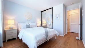 A bedroom with a large bed, bedside tables with lamps, a mirror, and a door with louvered shutters. - Luxurious Seabreeze Chic, 2 Bed Condo (Newport Beach)