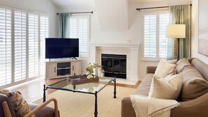 A living room with a TV, fireplace, sofa, and large windows. - Luxurious Seabreeze Chic, 2 Bed Condo (Newport Beach)