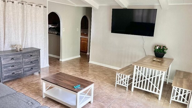 Ein modernes Wohnzimmer mit Deckenventilator, Flachbildfernseher an der Wand, Couchtisch aus Holz und grauem Sofa.