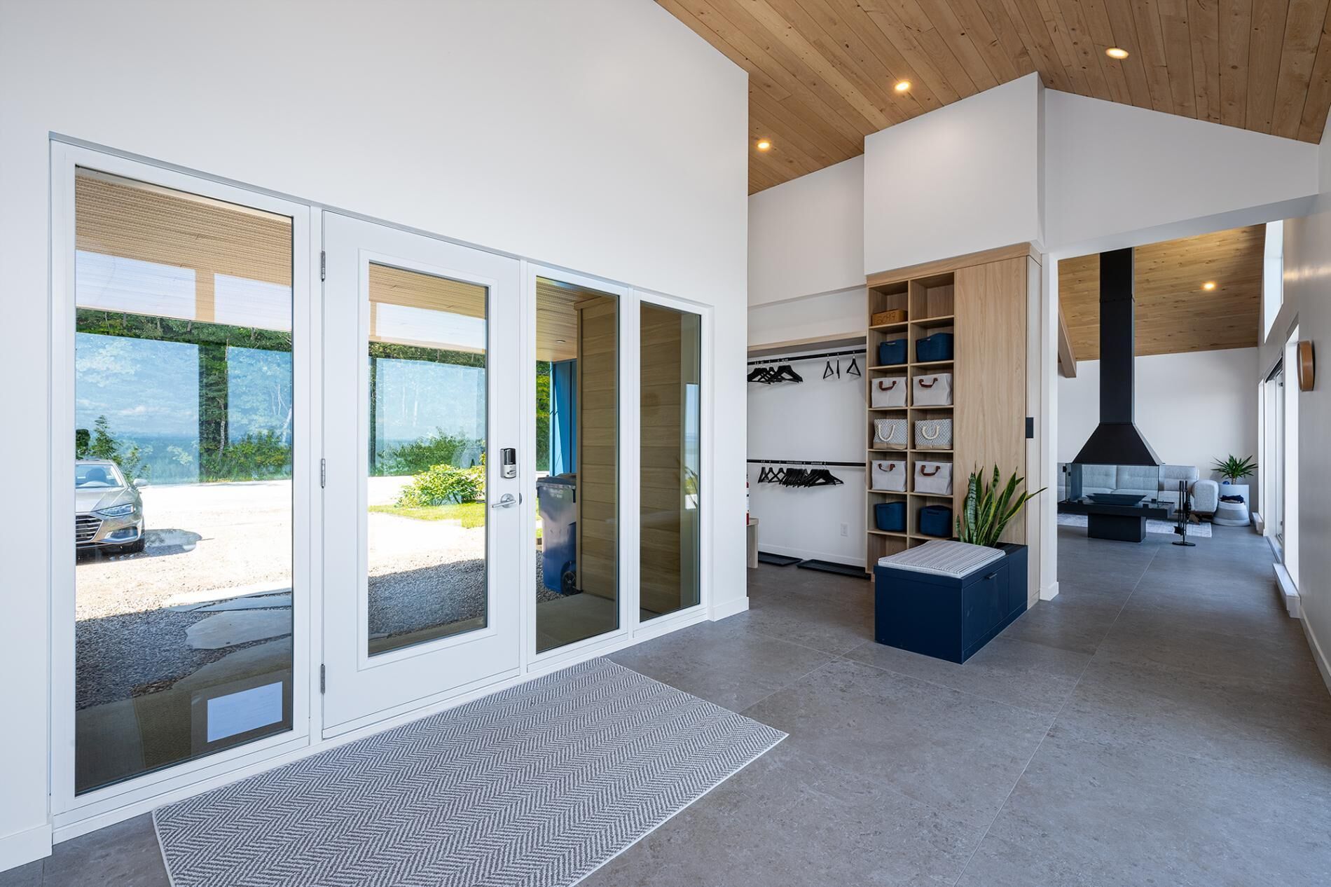 Un intérieur moderne avec une grande porte-fenêtre coulissante donnant sur une allée, un meuble à chaussures intégré et une cuisinière noire dans la cuisine.