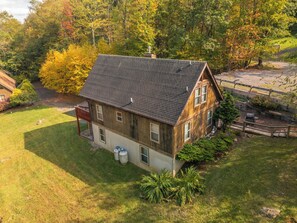 A two-story wooden house with a sloped roof, a fenced yard, and a small deck. - Swings, Lakeview A-frame + Hot Tub, 120” screen (Oakland)