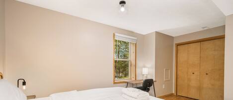 Ein Schlafzimmer mit einem großen Bett, einem Fenster mit Jalousien, einem Schreibtisch mit Stuhl und einem Kleiderschrank.