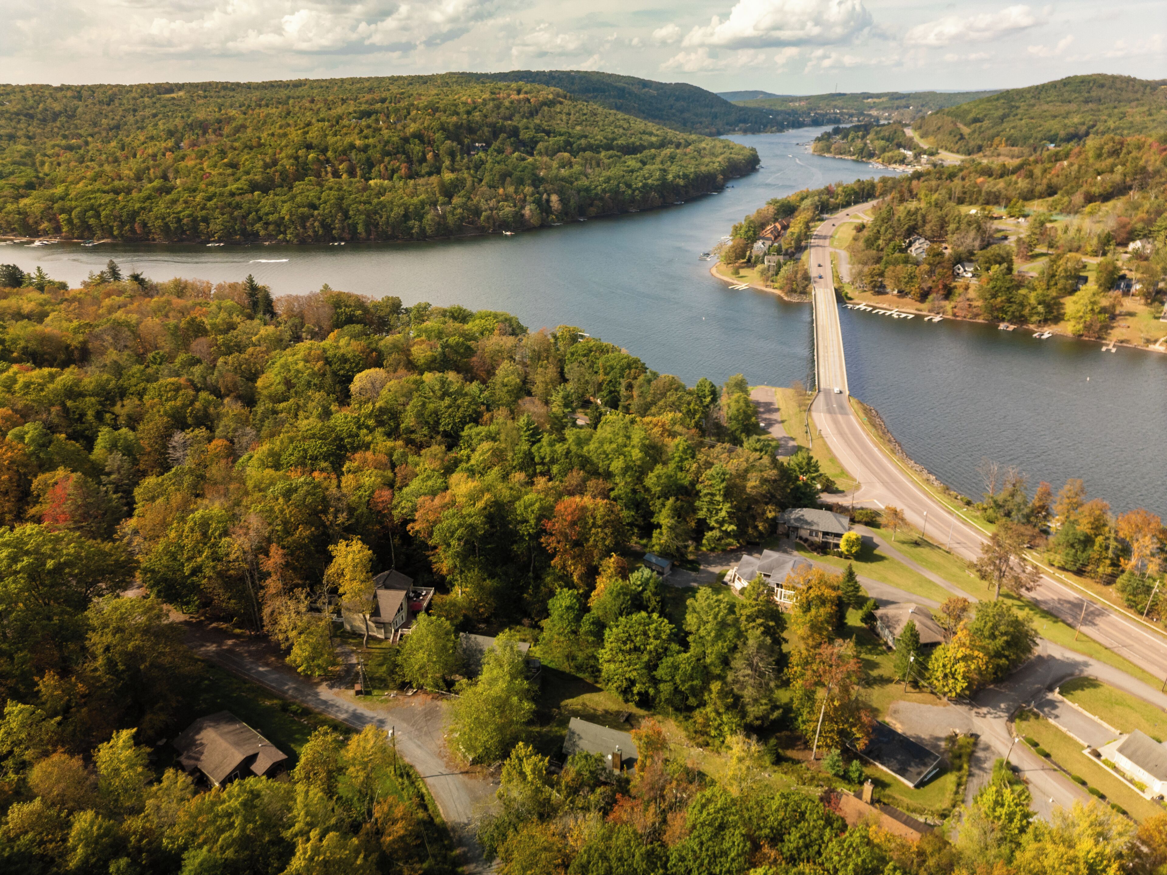 An aerial view of a residential area with a bridge over a river, surrounded by dense forests and houses.