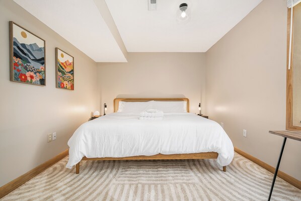 Un dormitorio con una cama, cabecera, mesita de noche, dos lámparas de pared y una lámpara de techo.
