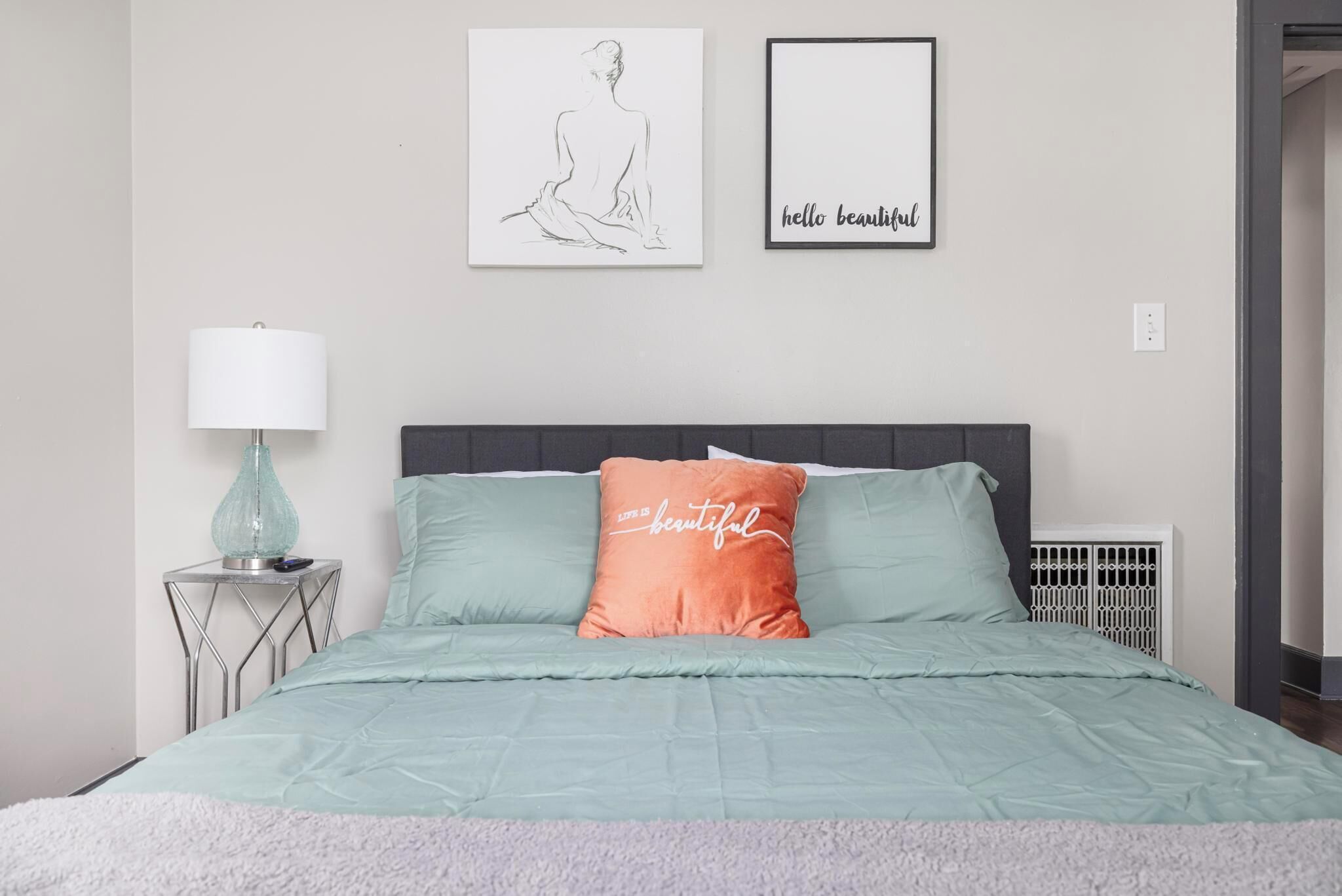 A bedroom with a bed, a bedside table with a lamp, and two wall art pieces.
