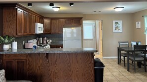 A kitchen with wooden cabinets, a granite countertop, a white refrigerator, and a dining area with a table and chairs. - New 2 bedroom home near Downtown (West Plains)