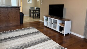 A living room with a wooden entertainment center, a flat-screen TV, a dining area with chairs, and a kitchen area with a refrigerator. - New 2 bedroom home near Downtown (West Plains)