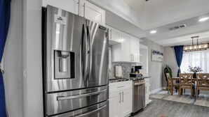 Una cocina moderna con electrodomésticos de acero inoxidable, armarios blancos y un comedor con mobiliario de madera.