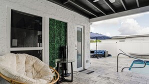 Un espacio exterior cubierto con piscina, una silla de mimbre, una mesa de cristal y una pared verde.