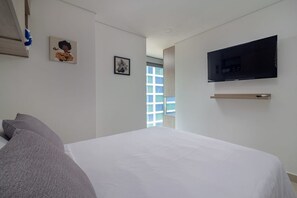 Une chambre à coucher avec un lit, un téléviseur fixé au mur et une fenêtre donnant sur un immeuble.