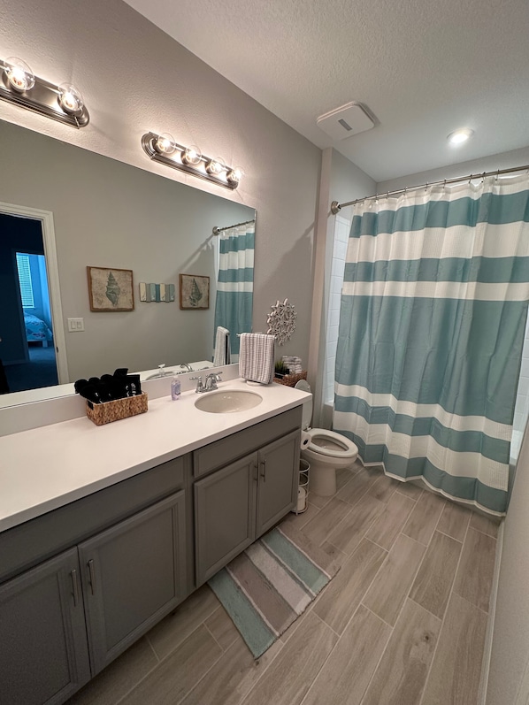 Une salle de bain avec un lavabo, un miroir et des toilettes. On trouve des objets décoratifs sur le comptoir et un rideau de douche à rayures.