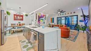 A modern kitchen with a marble island, wooden cabinets, and a dining area with a bench. There is a colorful rug and a ceiling fan. - Luxury 4BR Near BeltLine Hot Tub Game Room  Sleeps 10 (Atlanta)