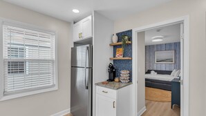 A compact kitchen with a refrigerator, a countertop with a coffee maker, and a small shelf with decorative items. - Professionally Managed | Walk to Beach (Seaside Heights)