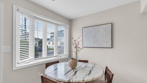 A dining area with a round marble table, four wooden chairs, a vase with flowers, and a wall-mounted abstract art piece. - Professionally Managed | Walk to Beach (Seaside Heights)